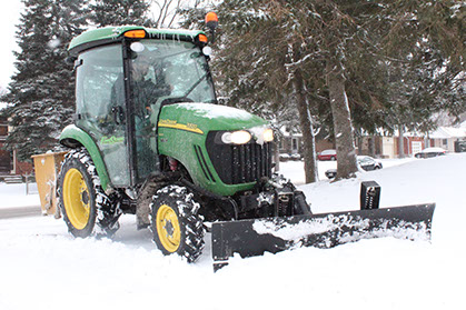 Green John Deere Tractor plowing snow on sidewalk
